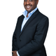 A man in a suit and shirt smiles.